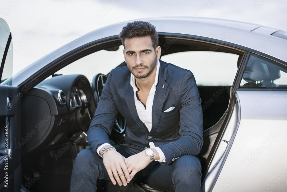 Portrait of young attractiave man in business suit sitting in his new stylish car outdoor in countryside Portrait of young attractiave man in business suit sitting in his new stylish car outdoor in countryside