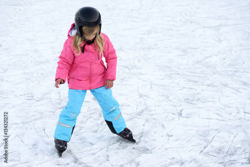 Happy little girl skating in winter outdoors, wearing safety helmet 