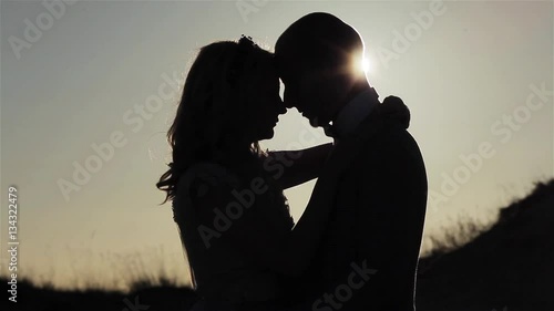Couple embrace silhouetted at sunset sly background close up. Man and woman contrast shadow pose outdoors standing together under golden hour sun ray beams shining. Parting tenderness relationship 
