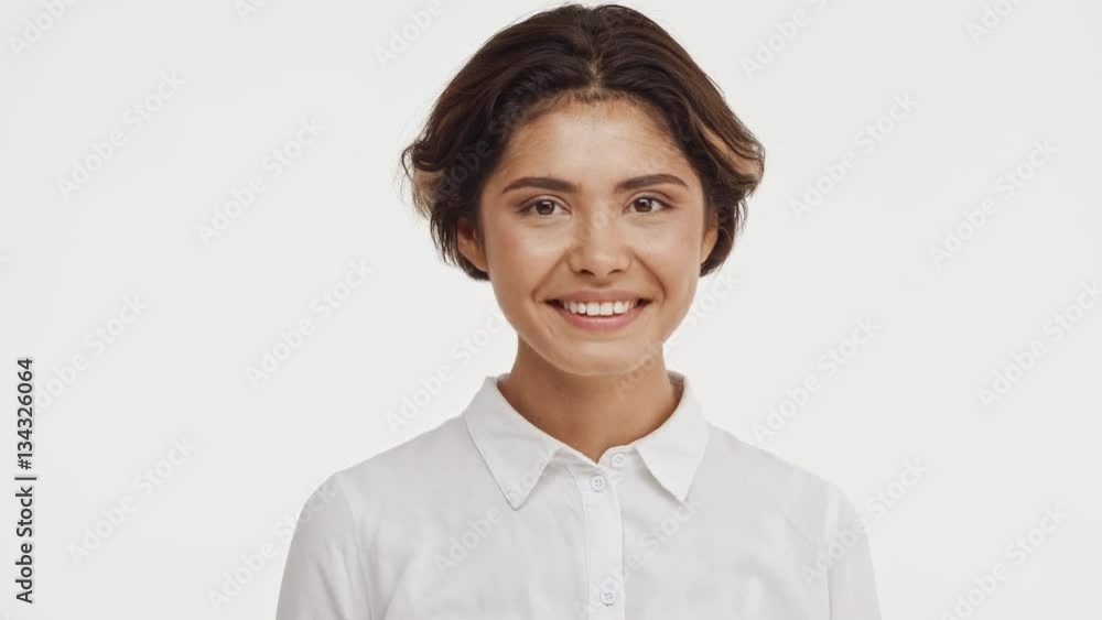 Young beautiful brunette east asian female in shirt snaping eyes at camera smiling laughing showing ok shaking head and hair on white background Young beautiful brunette east asian female in shirt snaping eyes at camera smiling laughing showing ok shaking head and hair on white background