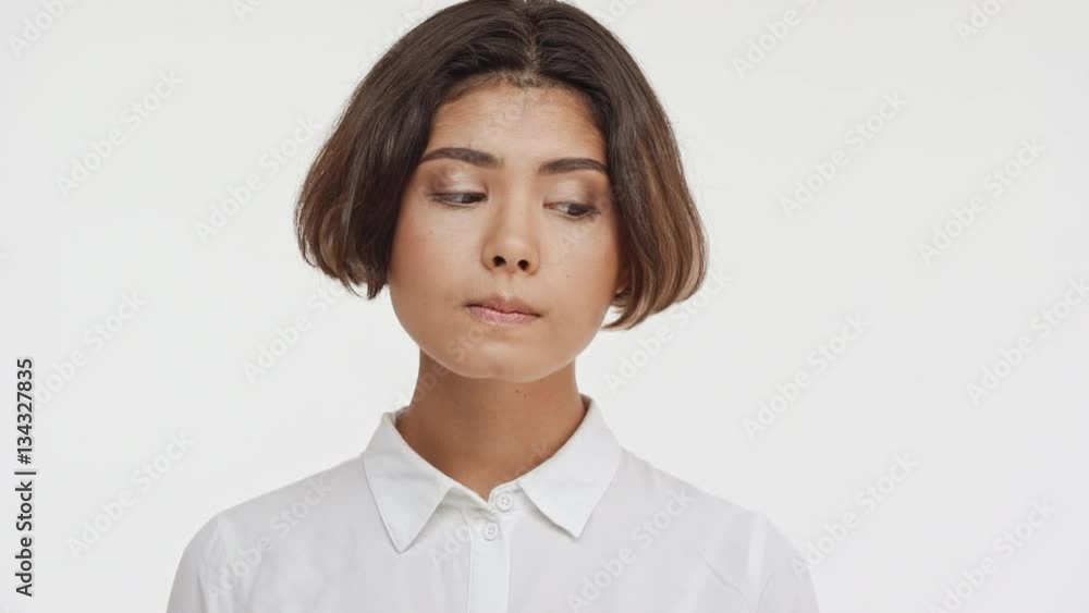 Young beautiful brunette east asian female in shirt standing on white background undecided shying in slowmotion Young beautiful brunette east asian female in shirt standing on white background undecided shying in slowmotion