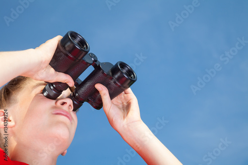 Boy looking through binoculars against blue sky