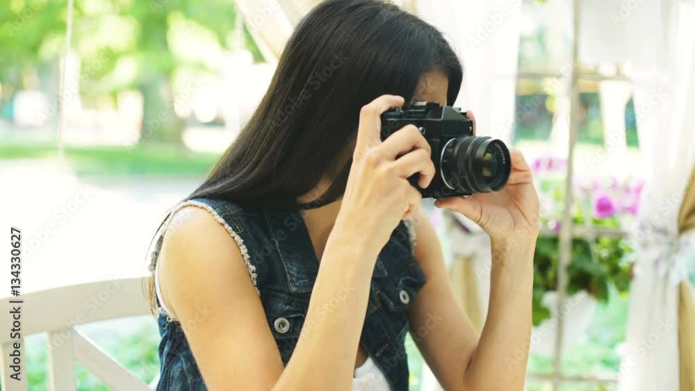 Beautiful young girl looking at viewfinder of camera and making photo while sitting in cage outdoors Beautiful young girl looking at viewfinder of camera and making photo while sitting in cage outdoors