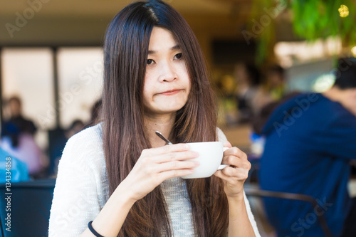 Student woman holding a cup of latte coffee in her hands at libr