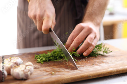 Ostrożne siekanie warzyw. Dłonie kucharza siekającego zioła na desce kuchennej