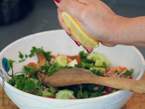 Hand squeezing lemon juice into a bowl of tuna salad.