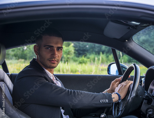 Handsome Young Man Driving a Car, wearing black jacket, hand on wheel © theartofphoto