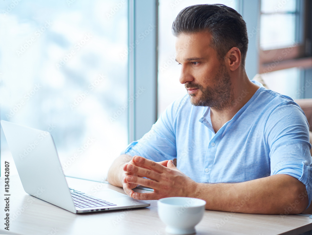 Handsome man with cup of coffee using laptop at home Handsome man with cup of coffee using laptop at home