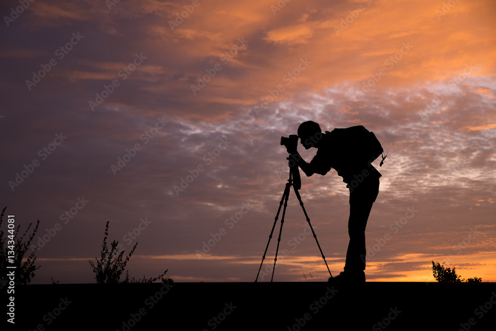 Silhouette of a photographer,he use a tripod.The background image is a sunset in Thailand.