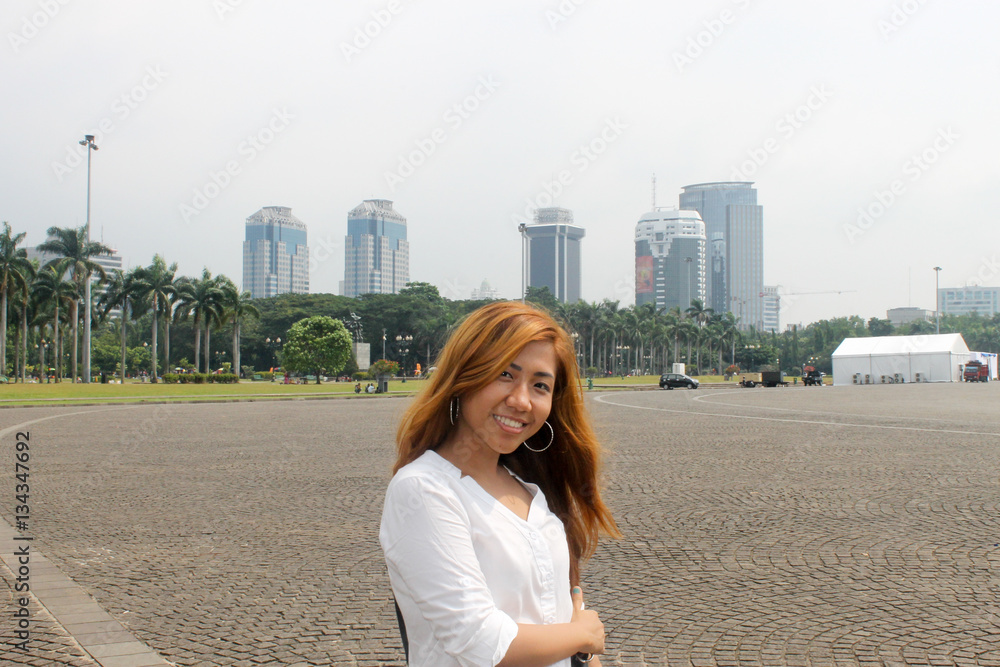 Asian girl posing in Monas, Jakarta with view of skyscrapers