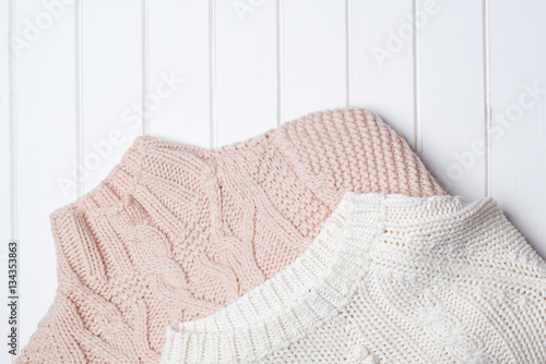 Two modern knitted sweaters on white wooden background.