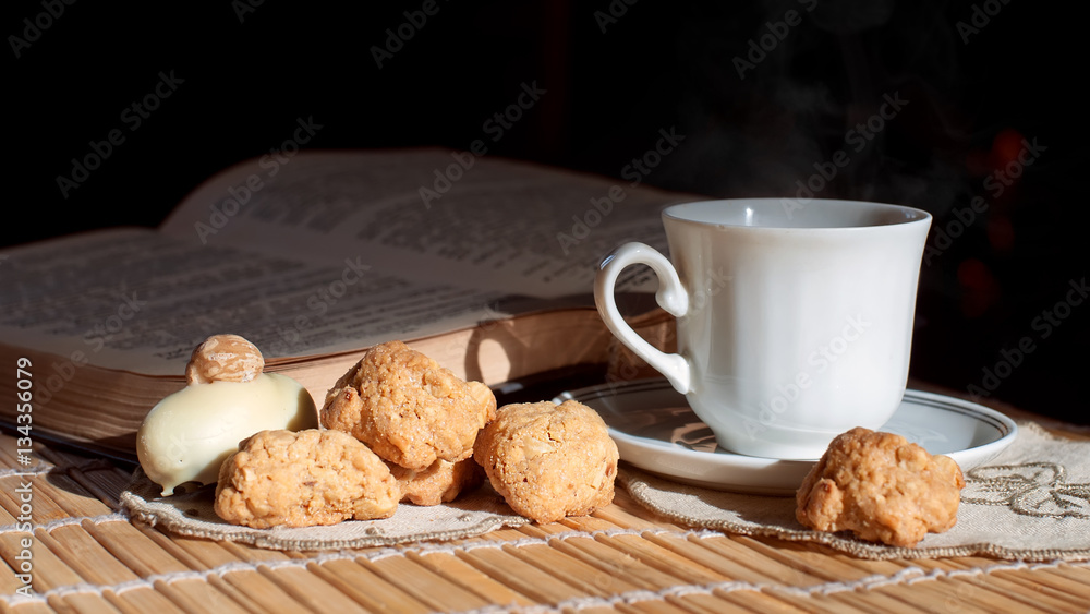 Still Life with a white cup of hot drink and fragrant biscuits on a background of an open book Still Life with a white cup of hot drink and fragrant biscuits on a background of an open book