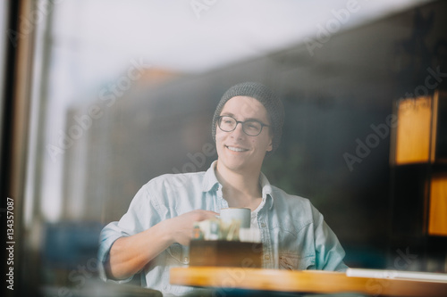 Handsome businessman in casual wear and eyeglasses is using a laptop in cafe