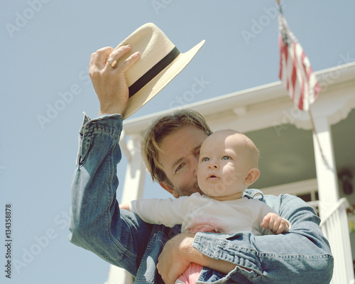 Father shading his baby boy from sunlight with hat