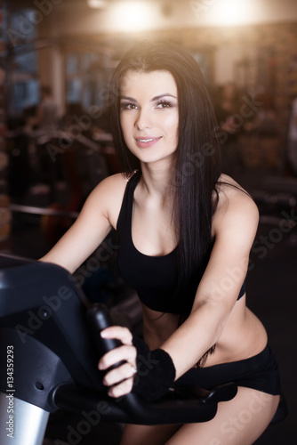 Muscular young woman wearing sportswear training on exercise bikes in gym. Intense cardio workout. © artyme
