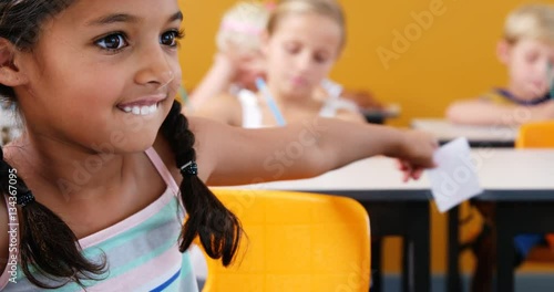 Schoolgirl giving chit to her friends in classroom at school 4k photo