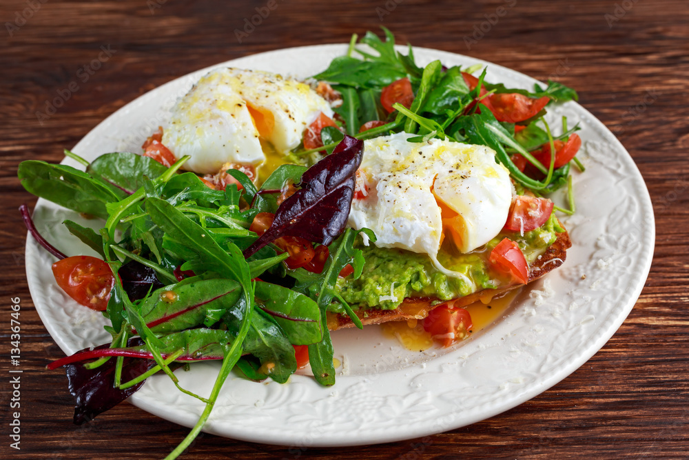 Smashed avocado and poached egg toast on green salad for breakfast