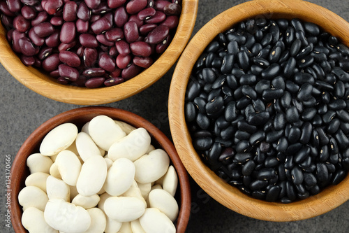 Black, purple and white dried beans in wooden bowls on a dark ru
