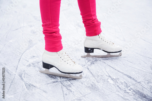 Woman skating and training with white skates on the ice area in winter day. Weekends activities outdoor in cold weather.