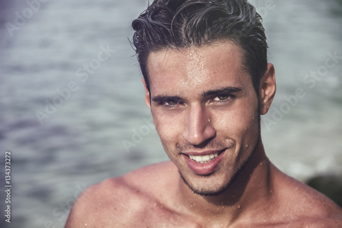Tablou pe pânză Attractive young man in the sea getting out of water with wet hair, looking in c