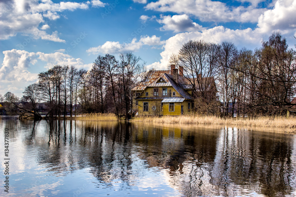 Landscape with old decaying and abandoned living house reflected in lake water.