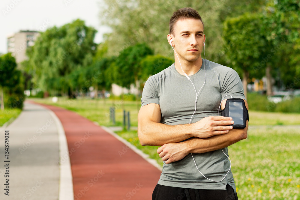 Fototapeta premium Outdoor runner man tuning his music player during jogging.