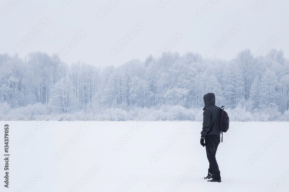 Young man walking and breathing fresh air in a white snowy countryside forest. Tree branches are snow covered. Winter day.