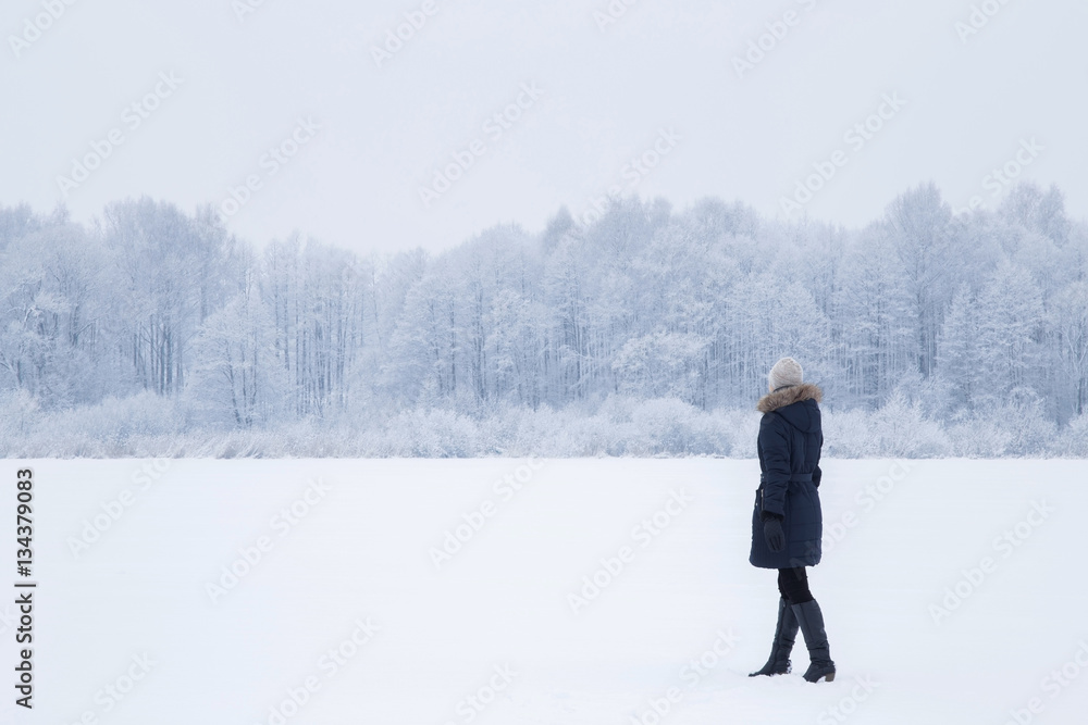 Woman walking and breathing fresh air in a white snowy countryside forest. Tree branches are snow covered.