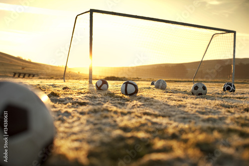 Soccer balls on an empty field at sunset