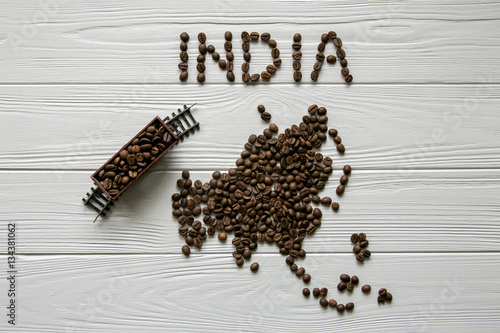 Map of the Indlia made of roasted coffee beans laying on white wooden textured background  with toy train