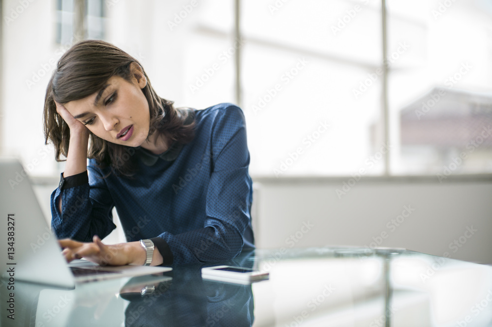 Frustrated young businesswoman working on her laptop in office Frustrated young businesswoman working on her laptop in office