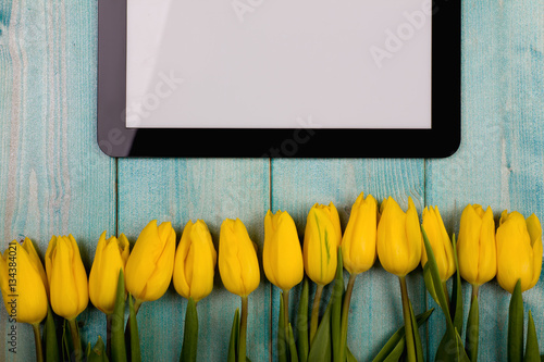 Fototapeta Naklejka Na Ścianę i Meble -  Yellow tulips and a wooden tablet on a blue background with sparkles