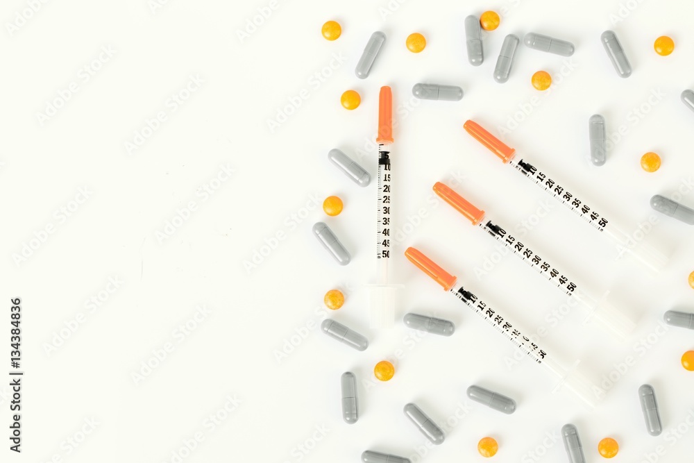 insulin syringe, pills and capsules on half of white background. insulin syringe, pills and capsules on half of white background.