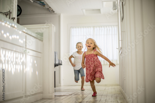 Two little girls have fun running through the house together.