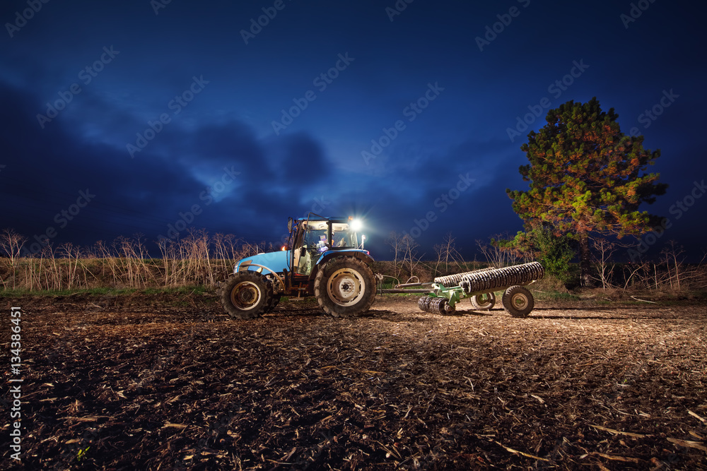 Obraz premium Tractor preparing land with seedbed cultivator at night
