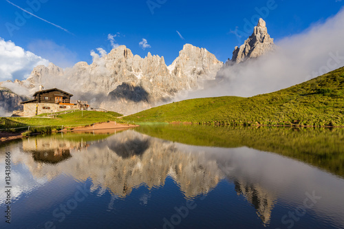 The Pale di San Martino peaks (Italian Dolomites) reflected in the water, with an alpine chalet on background. photo