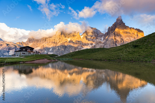 The Pale di San Martino peaks  Italian Dolomites  reflected in the water at sunset  with an alpine chalet on background.