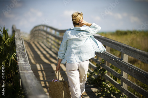 Mature adult woman walking along a wooden path towards the beach. photo