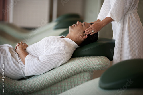 Man having head massage while lying on chaise lounge in a spa photo