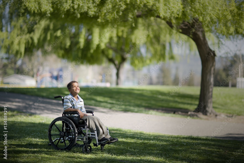 Smiling young boy sitting in a wheelchair at the park. Smiling young boy sitting in a wheelchair at the park.
