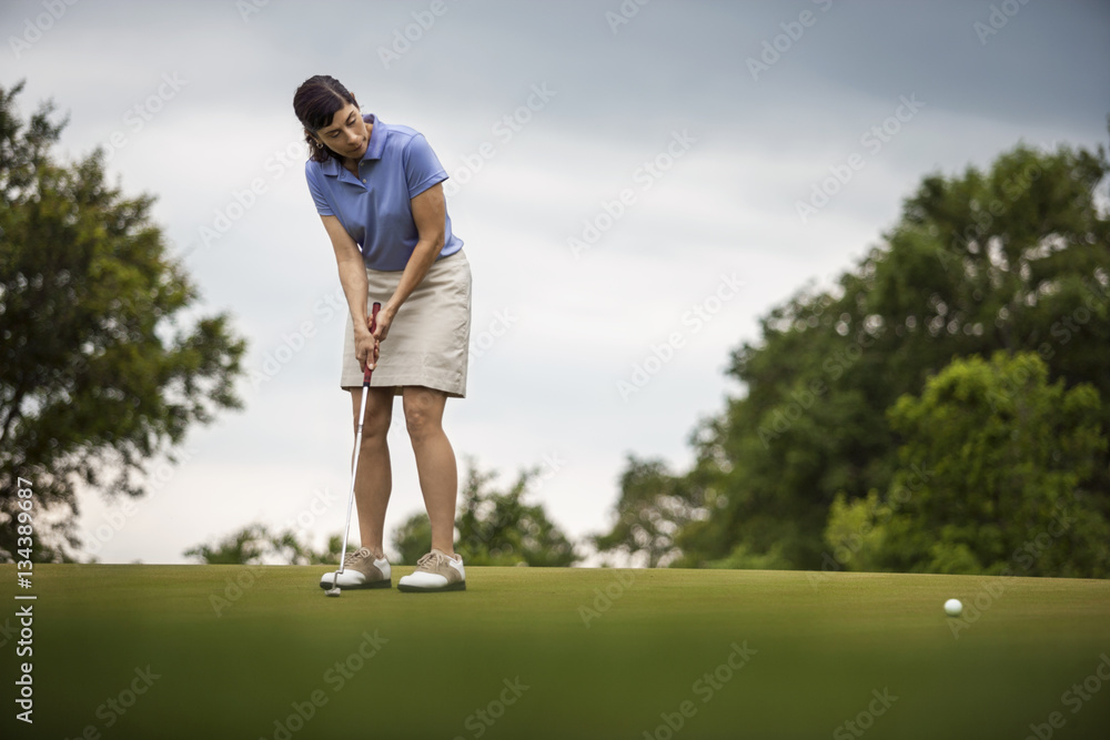 Mature woman looks on as she putts golf ball Mature woman looks on as she putts golf ball