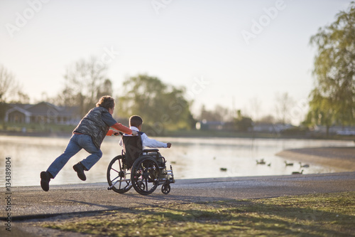 Boy pushing his friend in wheelchair through park