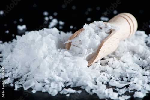 Salt flakes and wooden scoop on black background photo