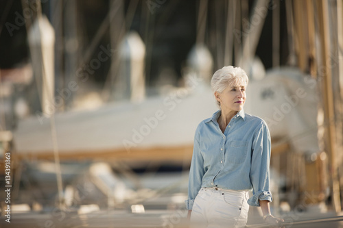 Senior woman wearing chambray shirt stands looking out at a marina. photo