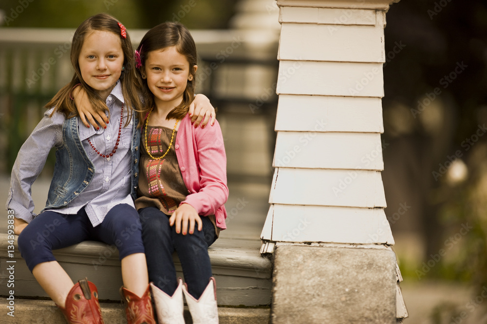Two young girls with their arms around each other sit together on the ...