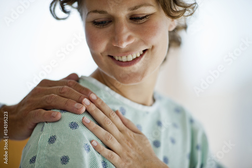 Female hospital patient smiling as she touches the comforting hand laid on her shoulder.