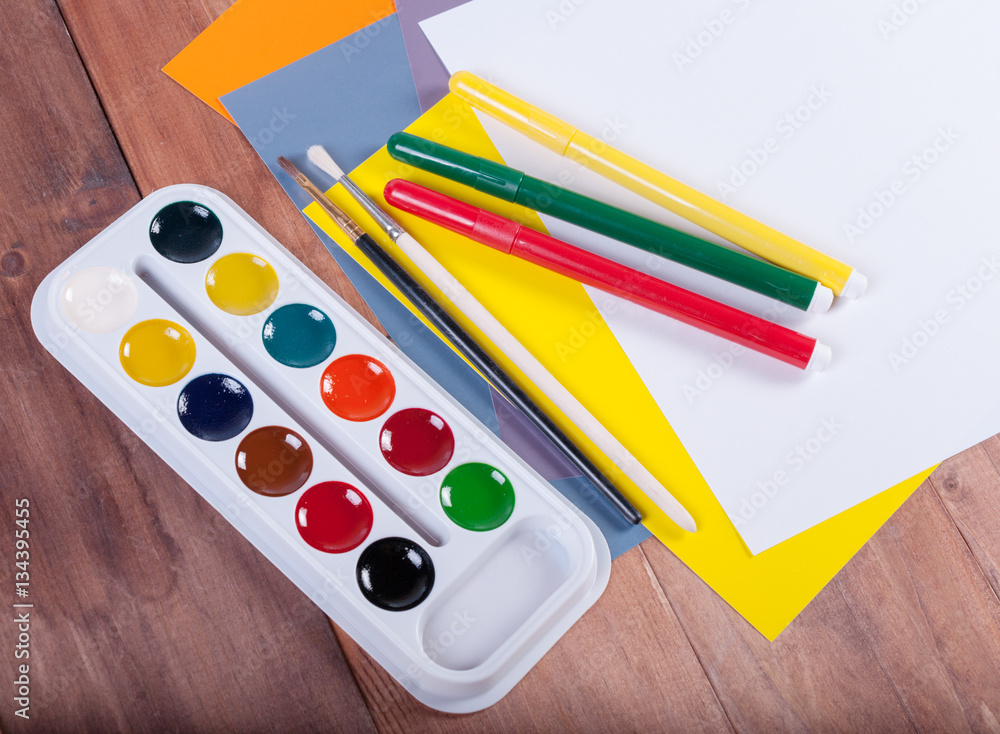 Naklejka premium Paper, watercolors, paint brush on wooden table