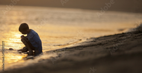 Young boy sitting with his leg in the water at a beach.