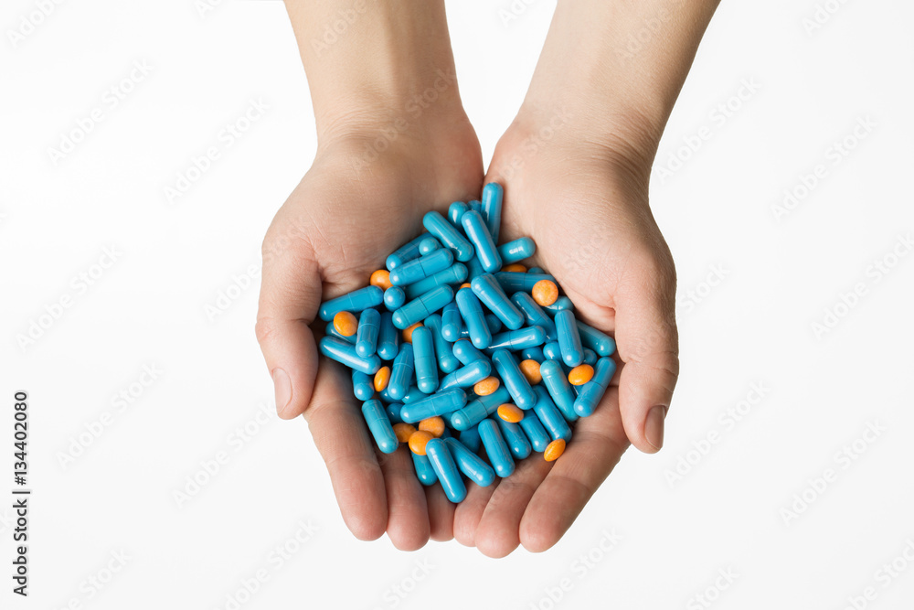 Hands is giving blue capsules and orange pills on white background. Hands is giving blue capsules and orange pills on white background.
