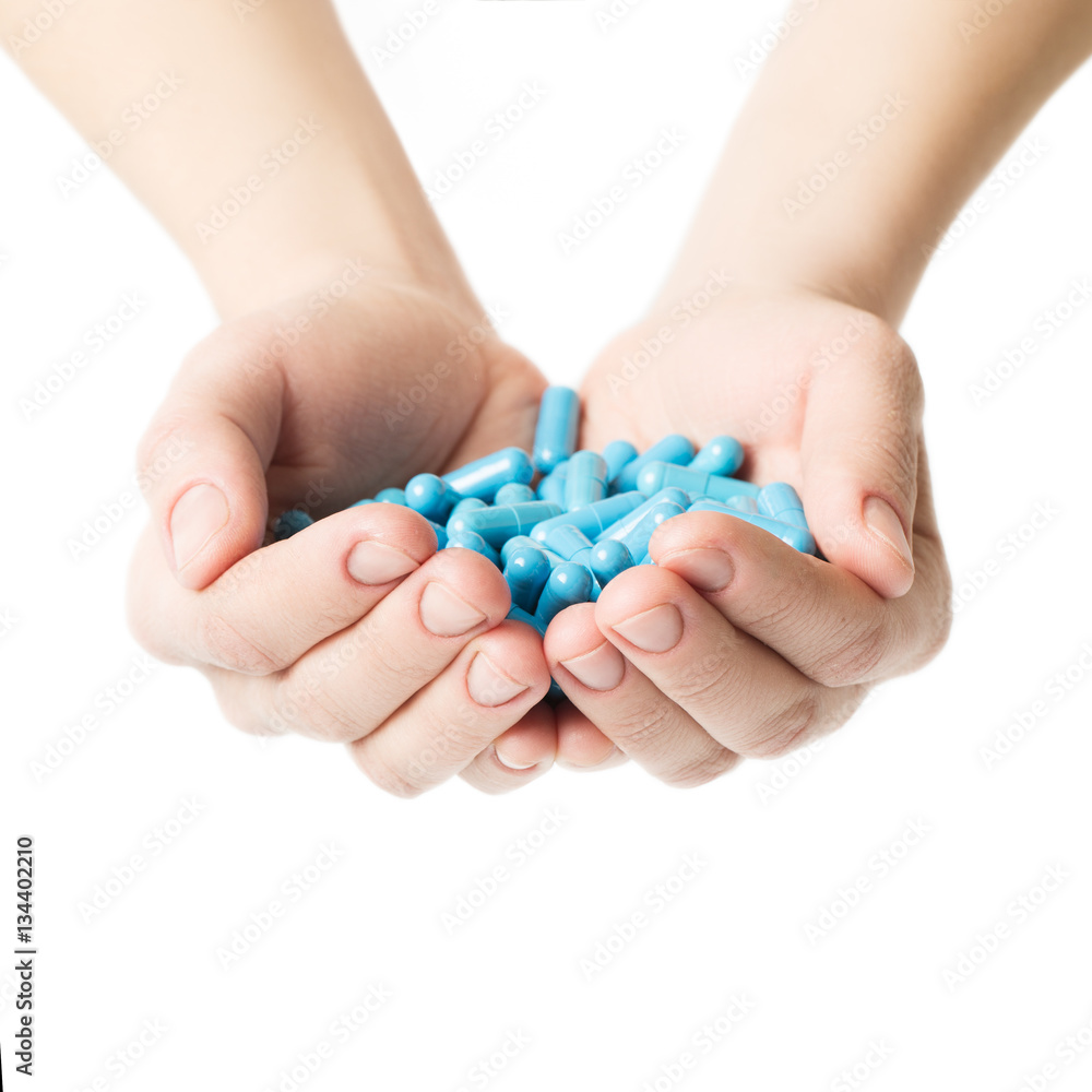 Hands is giving blue capsules and orange pills on white background.